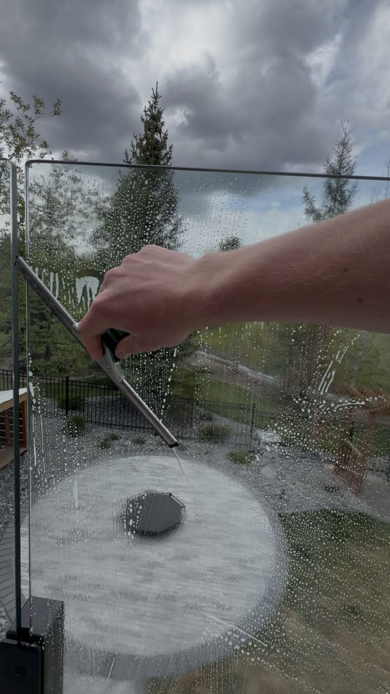 Squeegee cleaning glass with sunlight catching a rainbow in the soap